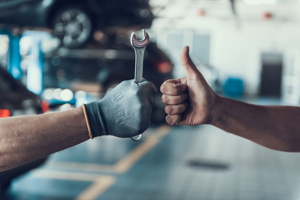 Two mechanics are giving each other a thumbs up while holding a wrench.