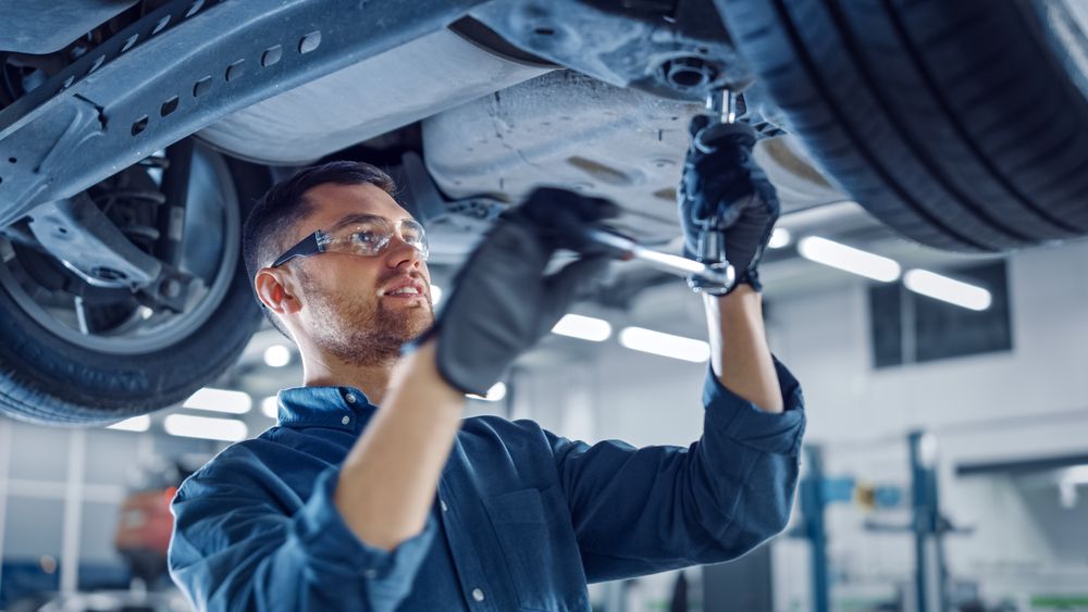 A man is working under a car with a wrench in a garage.