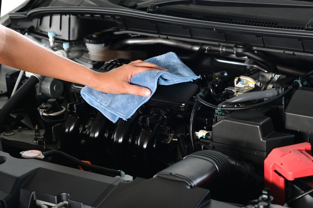 A person is cleaning the engine of a car with a towel.