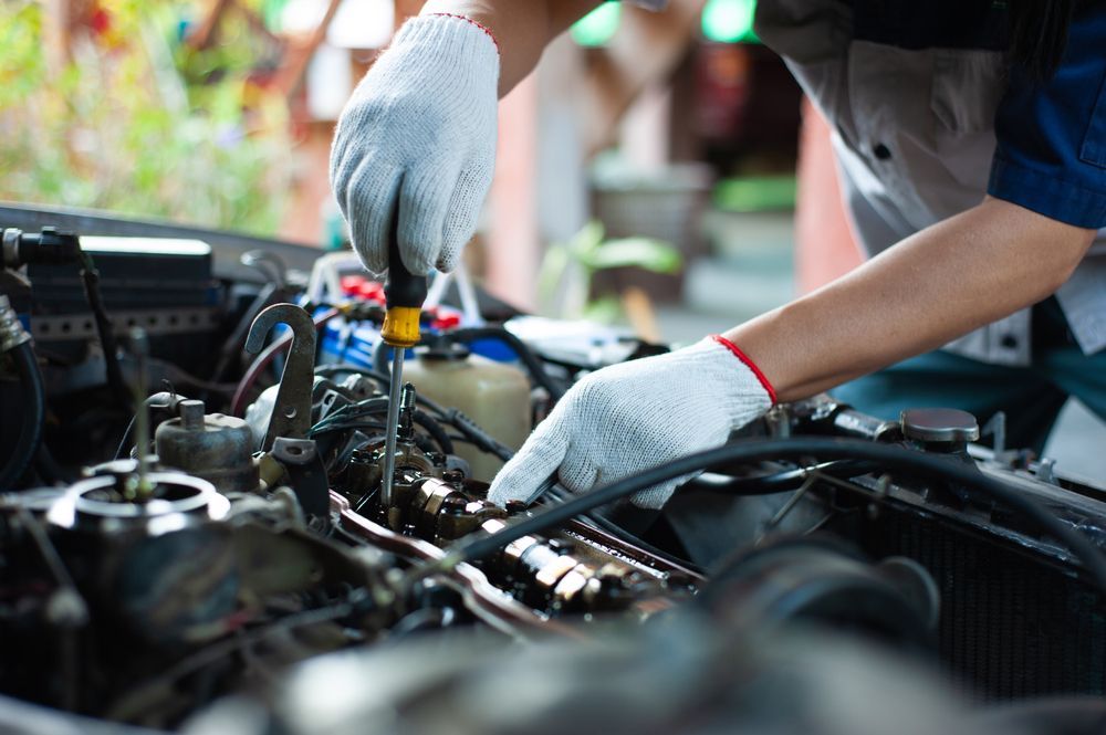 A man is working on a car engine with a screwdriver.