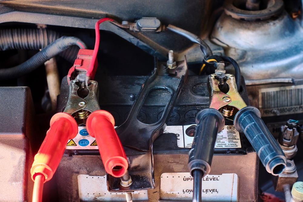 A close up of a car battery with jumper cables attached to it.