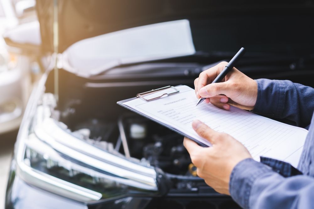 A man is writing on a clipboard in front of a car.