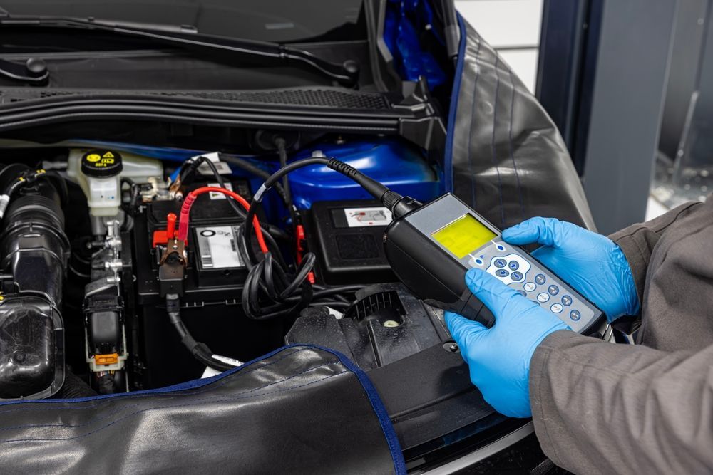 A person wearing blue gloves is working on a car battery.