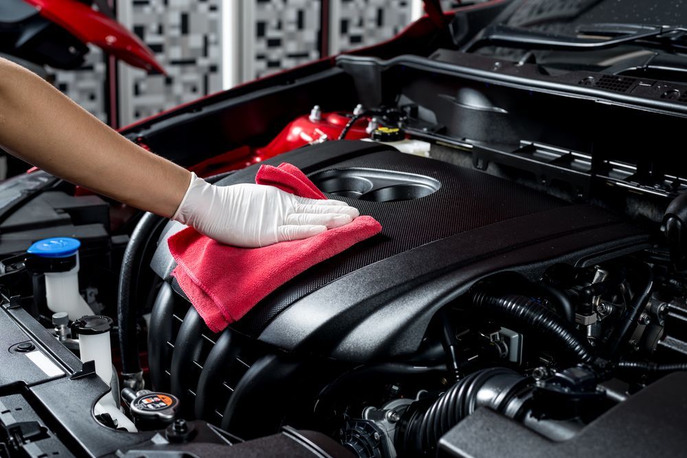 A person is cleaning the engine of a car with a cloth.