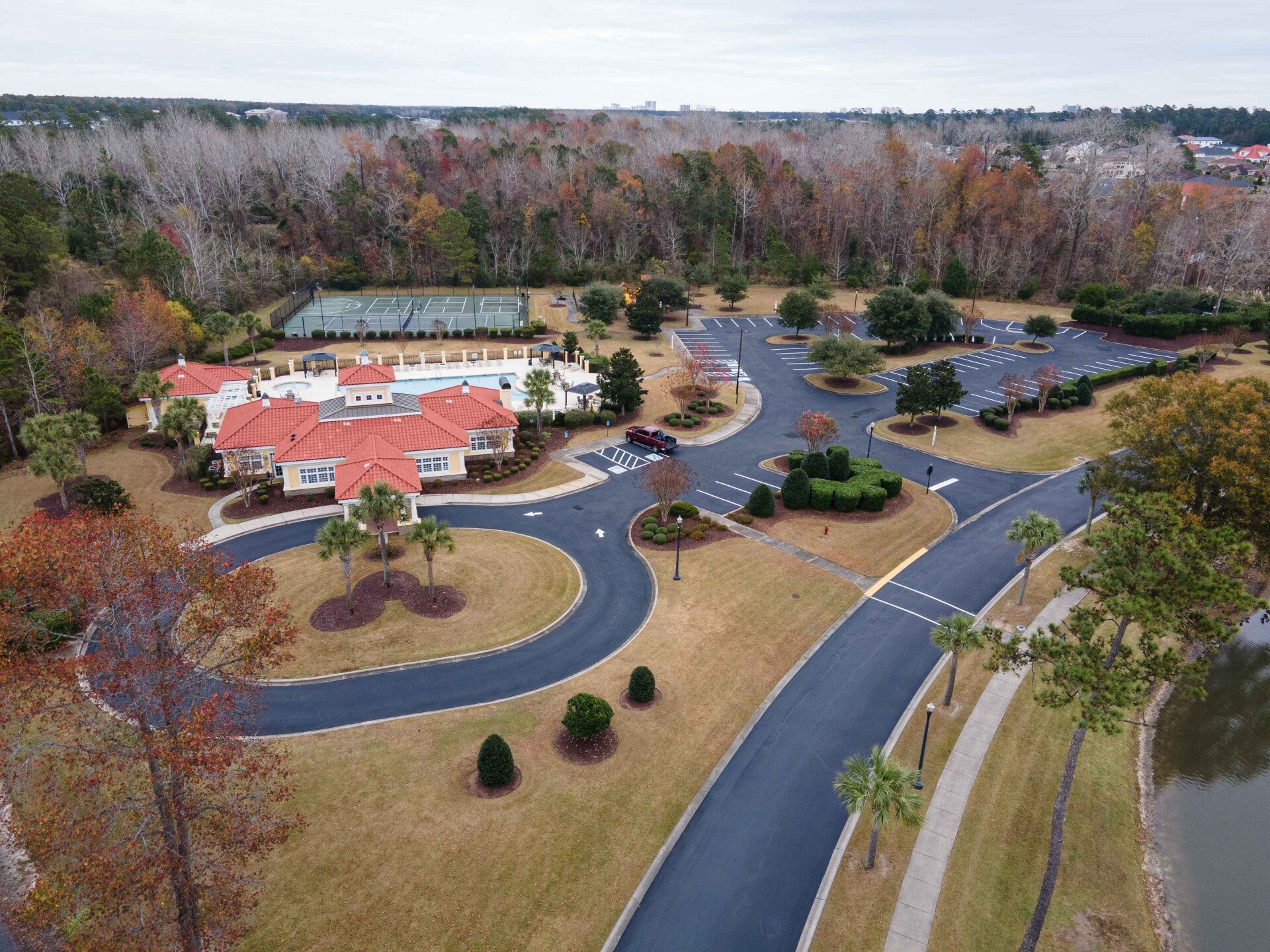An aerial view of a residential area with a tennis court and a lake.