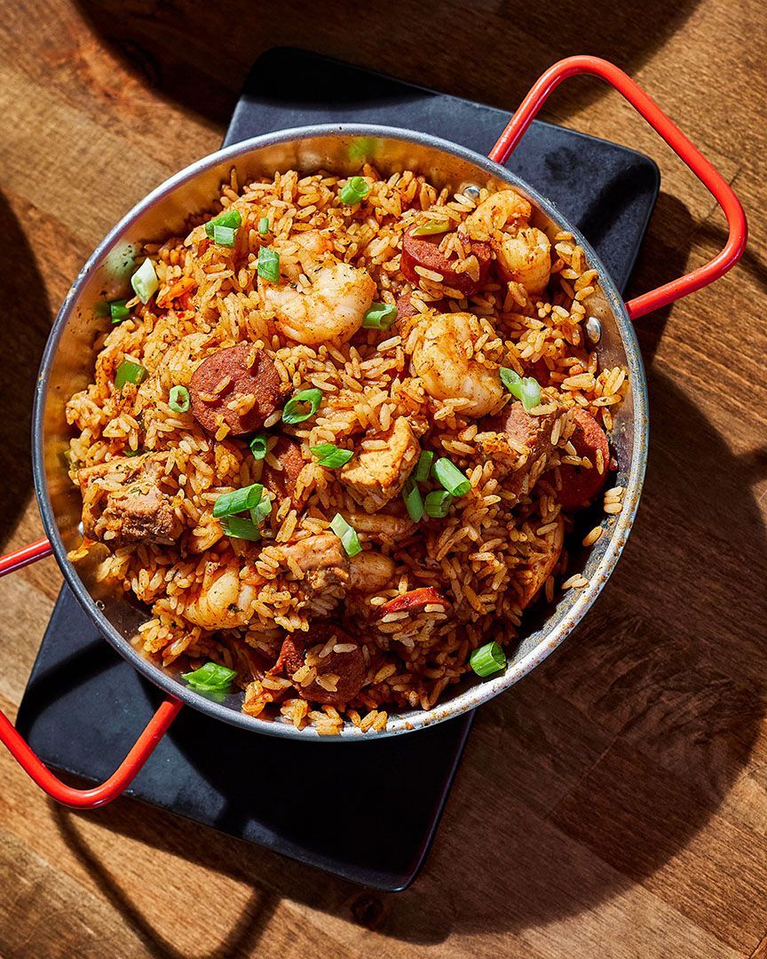 Jambalaya with shrimp, sausage, and chicken in a metal dish with red handles, on a black napkin on a wooden table.
