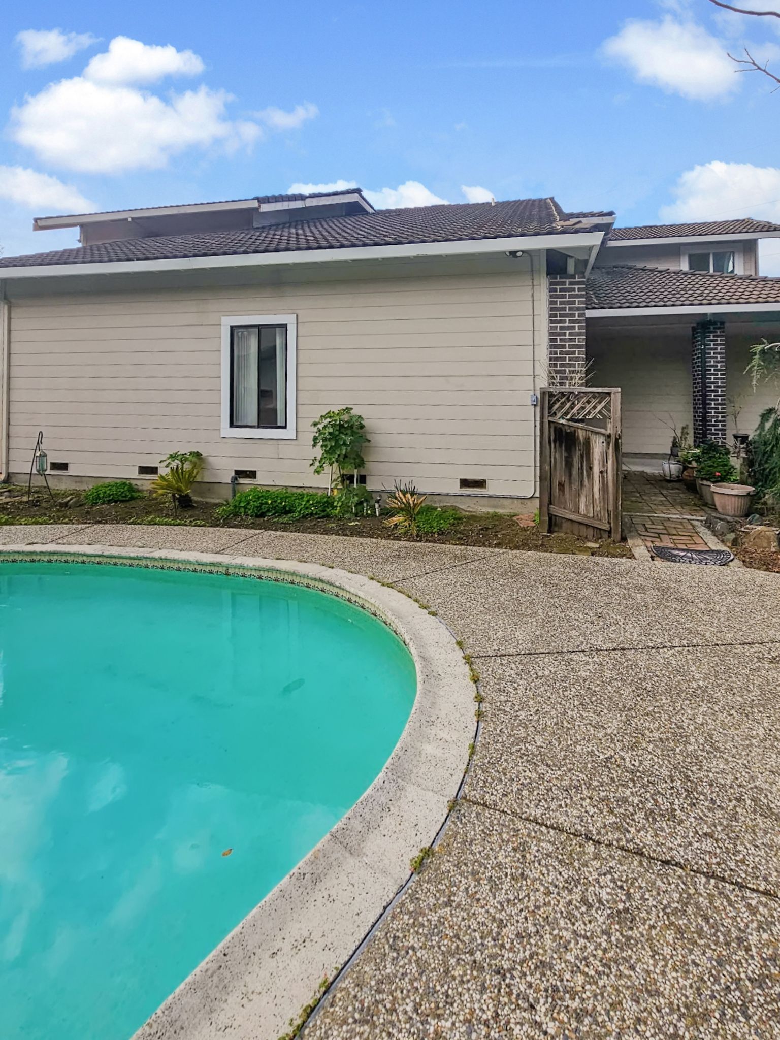 A light-tan, two-story house with a bay window, glass patio doors, and a decorative concrete patio in the backyard.