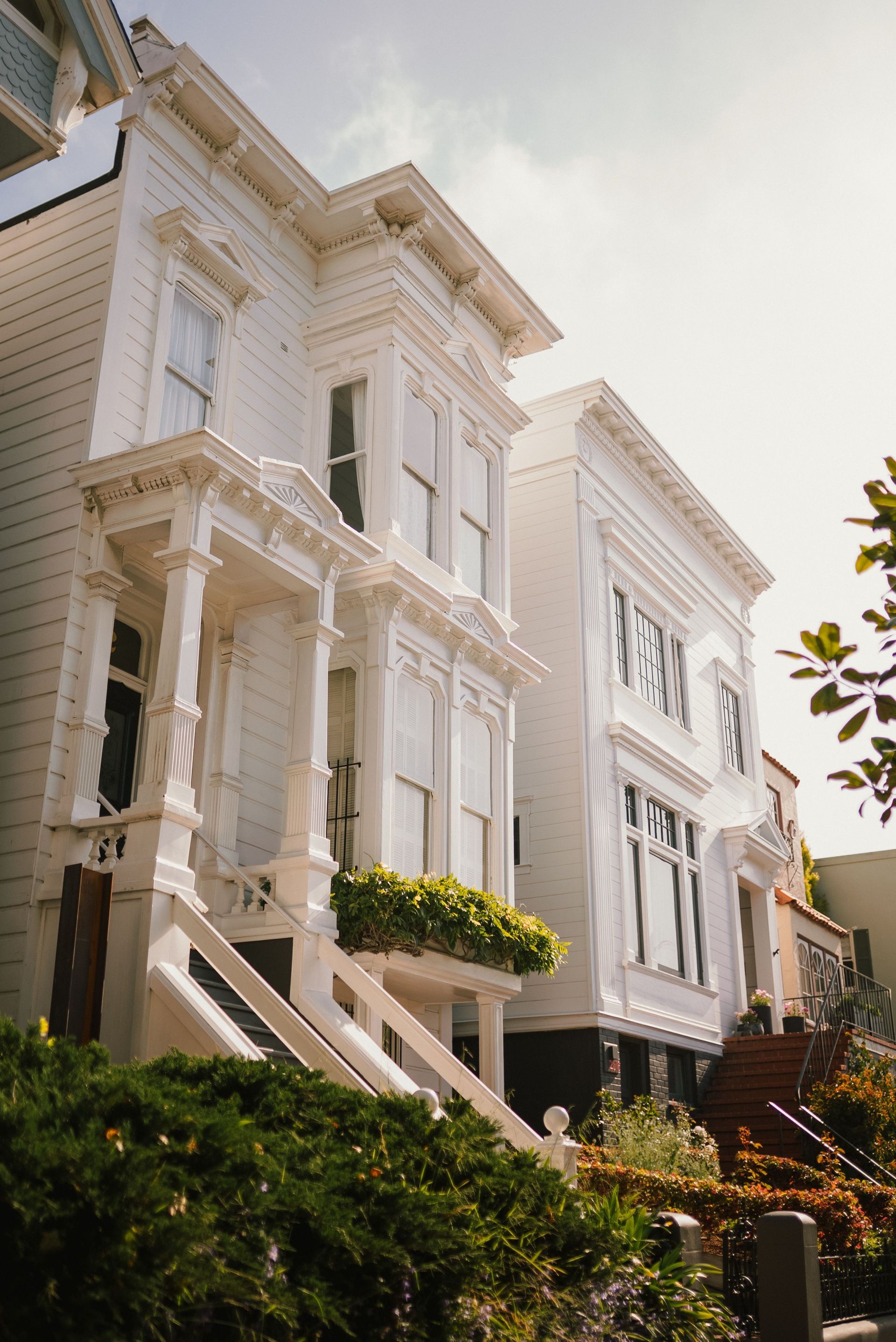 White Victorian-style row houses with ornate facades on a sunny street, viewed from below.