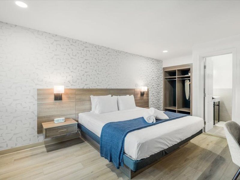 Modern bedroom with white bed, blue throw, nightstands, and open closet in a bright, minimalist room