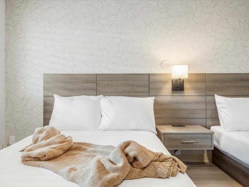 Modern hotel room with two white beds, wood headboard, and a wall lamp