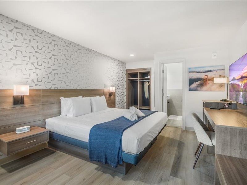 Modern hotel room with a large bed, desk, chair, wood flooring, and wall art