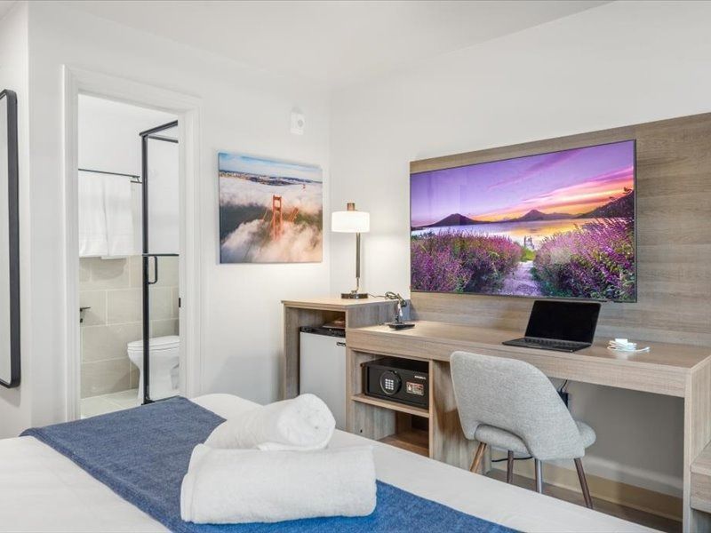 Modern hotel room with twin beds, desk, wall-mounted TV, and open bathroom door