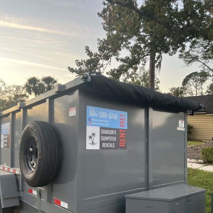 A dumpster with a tire on the back is parked in a yard.