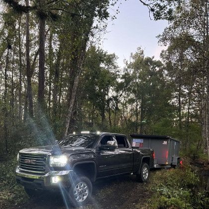 A gmc truck is parked in the woods with a trailer attached to it