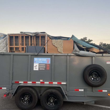 A dumpster trailer filled with junk is parked in a parking lot.