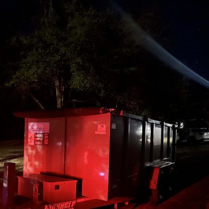 A red dumpster is parked next to a tree at night.