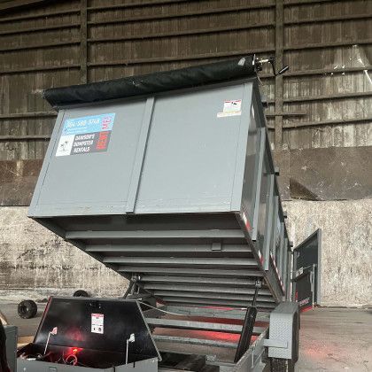 A dumpster is sitting on top of a trailer in a warehouse.