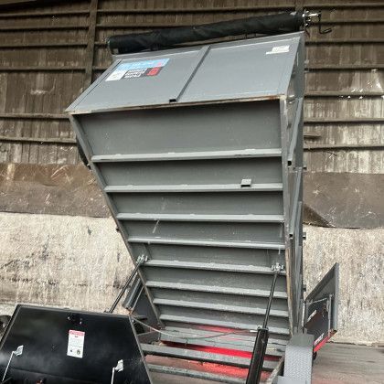 A dumpster is sitting in front of a wall with the lid open