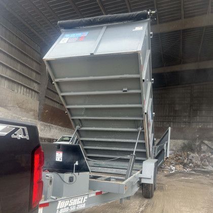 A dumpster trailer is parked in a warehouse next to a truck.