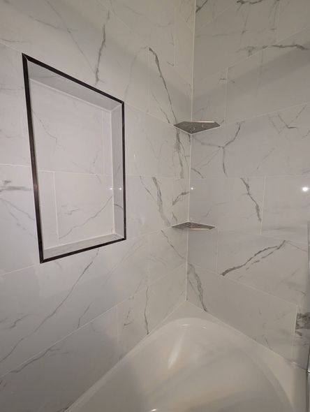 White tiled shower with built-in shelf and recessed niche. The shower has a marble-like pattern.