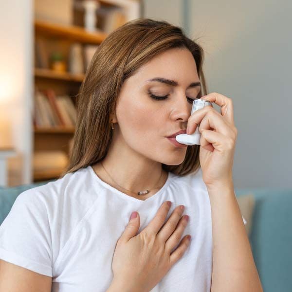 A woman is using an inhaler to treat her asthma.