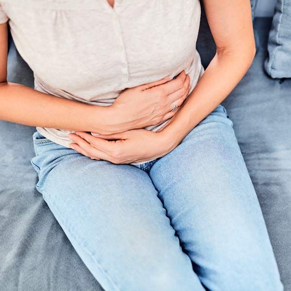 A woman with Autoimmune Deficiency is sitting on a couch with her hands on her stomach.
