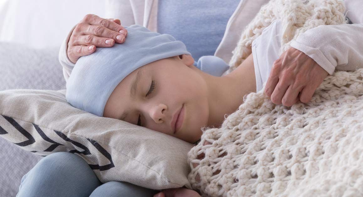 A child with cancer is sleeping in a bed with a person holding his head, waiting for Blood Disorder Treatments NJ and NYC - Victory Medical Institute