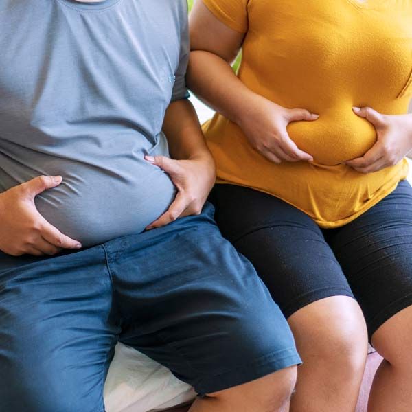A man and a woman sit next to each other, their hands on their stomachs. Prime candidates for Advanced Medical Body Contouring with EvolveX Serving Patients in Morris Plains New Jersey and Manhattan New York