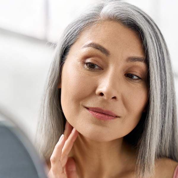 A woman with gray hair is looking at her face in a mirror after her Medical Botox Injections in Morris Plains New Jersey and Manhattan New York