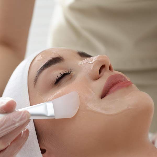 A woman is getting a facial treatment with a brush representing Chemical Peels - Medical-Grade, whichreveals yourr Inner Glow