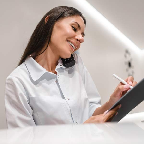 A woman is smiling while talking on a cell phone and writing on a clipboard for a new patient interested in Proven Medical Diet and Detoxification Plans, in Morris Plains, New Jersey, and Manhattan, New York