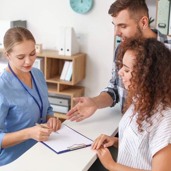A man and a woman are sitting at a desk talking to a nurse after Contact Victory Medical for an Emerging Therapy Consultation