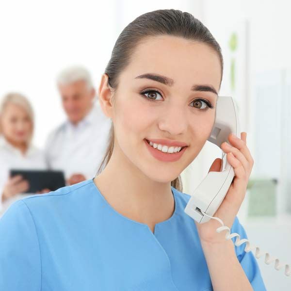 A medical receptionist in a blue scrub is talking on a phone with a person interested in Medical Peptide Injections in Morris Plains, New Jersey, and Manhatta,n New York