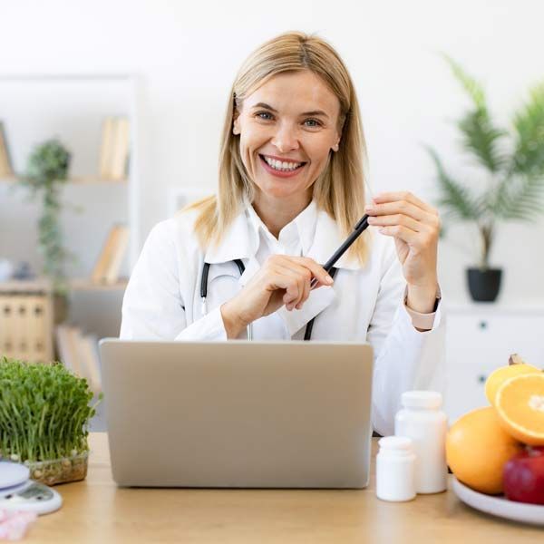 A female doctor is sitting at a desk with a laptop computer, offering Coaching and Wellness Weight Loss Support services to patients