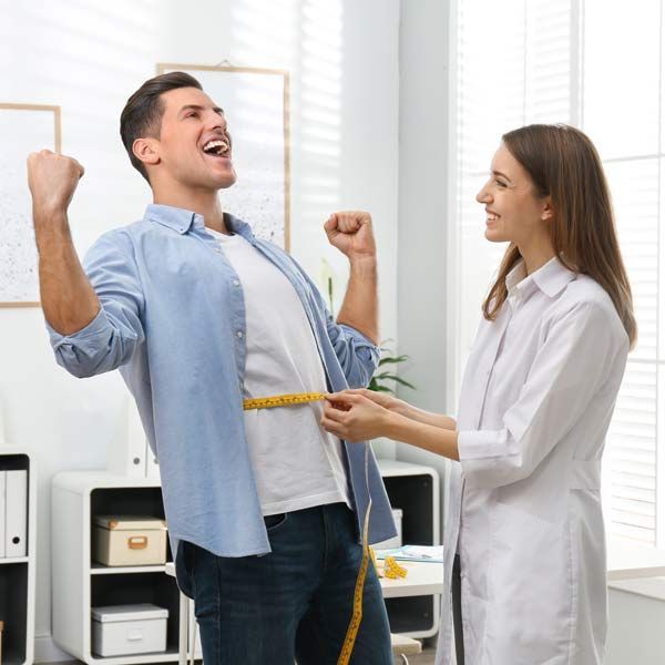 A woman is measuring a man's waist with a tape measure, showing a successful diet plan.