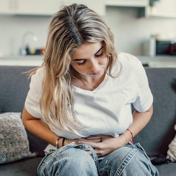 A woman with Digestive Disorders is sitting on a couch holding her stomach.