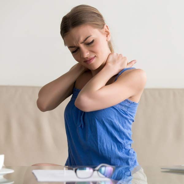 A woman with Fibromyalgia is sitting at a table with her hand on her neck.