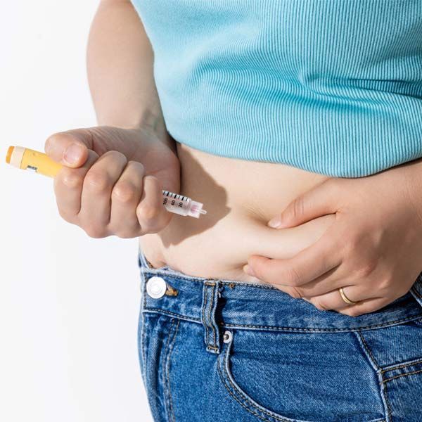 A woman is holding a GLP-1 Therapy syringe to her stomach.
