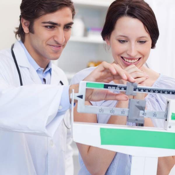 A doctor and a woman are looking at her weight on a scale
