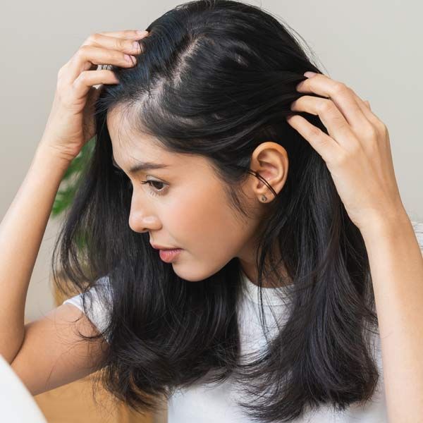 A woman in a white shirt is touching her hair, needing Advanced Hair Regrowth Solutions, Serving Patients in Morris Plains, New Jersey, and Manhattan, New York