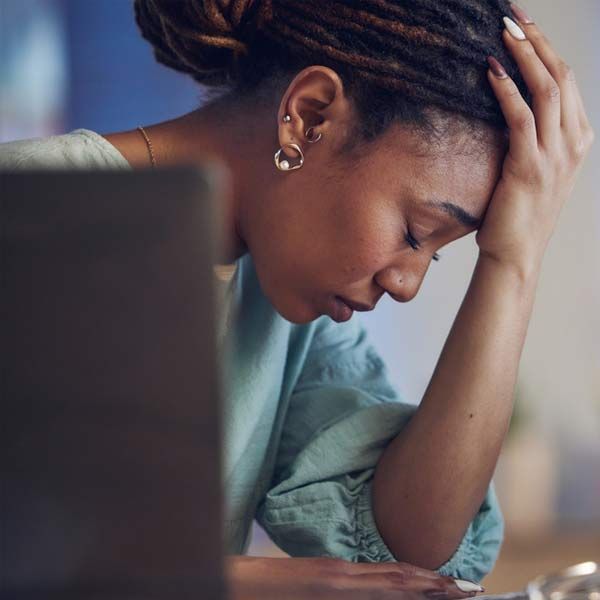 A woman is sitting at a desk with Headaches and her head in her hands.