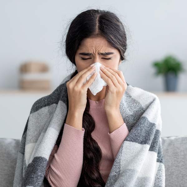 A woman is blowing her nose with a napkin while wrapped in a blanket representing Immune Defence IV Therapy