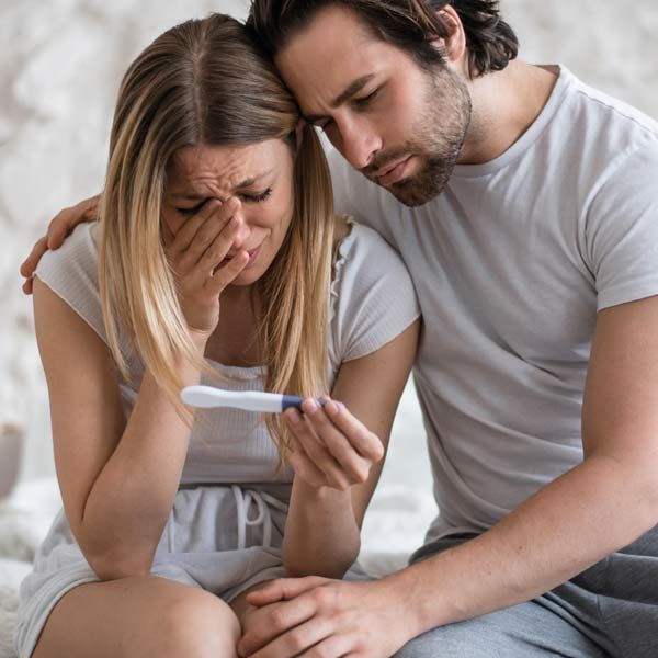 A man is comforting a woman who is crying while holding a negative pregnancy test due to Infertility.