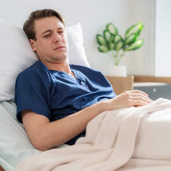 A man with Long Covid in a blue shirt is laying in a hospital bed