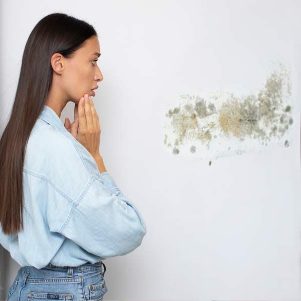 A woman is standing in front of a wall with mold on it, representing Mold Exposure and Toxicity Detox