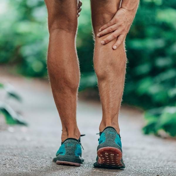 A man is holding his calf in pain while walking down a path representing Muscle Cramp Relief IV therapy
