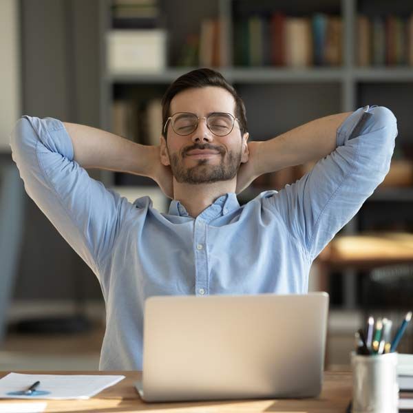 A man is sitting at a desk with his hands behind his head in front of a laptop computer with energy from his Myers Cocktail