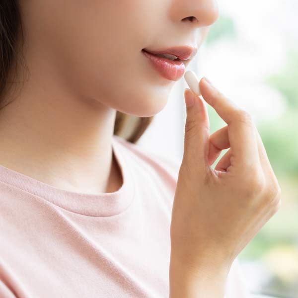 Woman in a pink shirt taking a white supplement for her Premenstrual Dysphoric Disorder Therapy Serving Patients in Morris Plains, New Jersey, and Manhatta,n New York