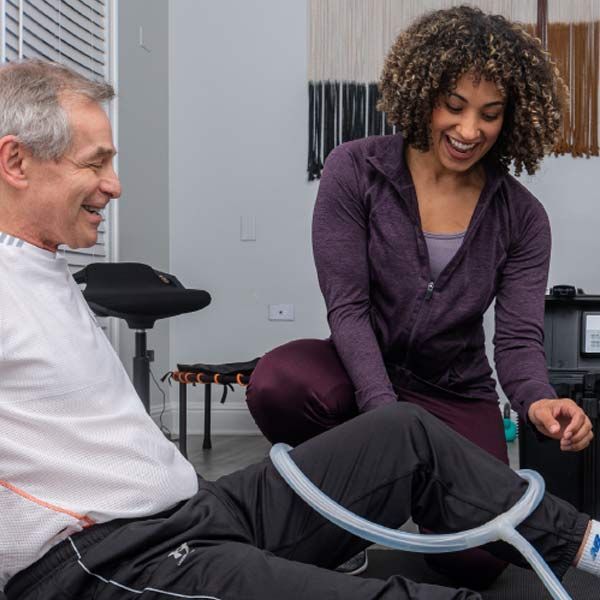 A woman is helping a man with a Pulsed Electromagnetic Field (PEMF) Therapy hose on his leg