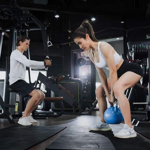 A man squatting next to a woman lifting a kettlebell in a gym represents Pre and Post Workout IV Therapy